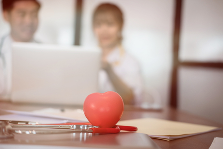 red heart & stethoscope on desk with doctor discussing patient treatment. medical staff have meeting for diagnosis plan in conference room in hospital.の写真素材