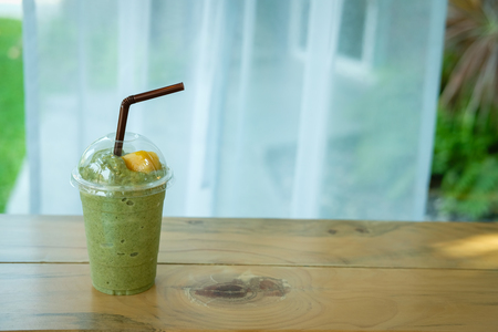 matcha green tea latte smoothie on wood table near window. delicious blended frappe beverage with mango. healthy dessert for summerの写真素材