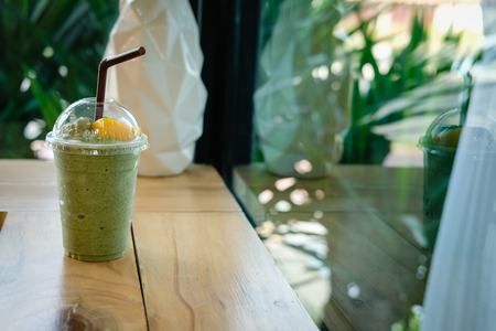 matcha green tea latte smoothie on wood table near window. delicious blended frappe beverage with mango. healthy dessert for summerの写真素材