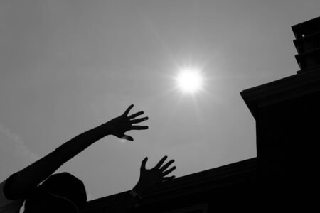 woman's hand reaching out for the sun with silhouette of modern buildingの写真素材