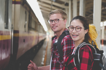 man and woman with backpack waiting for train at railway station. loving couple traveler travel together on holidayの写真素材