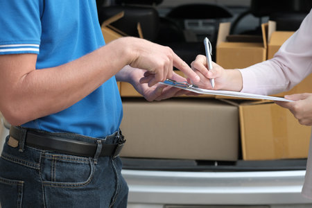 woman signing signature on clipboard to receive package from delivery man. male postal courier...