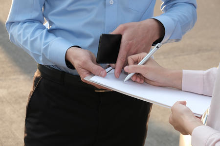 man agent examining car damaged by traffic accident. woman filling auto insurance form & signing signatureの写真素材