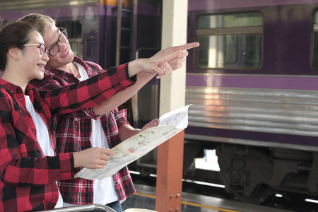 man and woman look at map while waiting for train at railway station. loving couple traveler travel together on holidayの写真素材