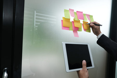Businessman write on adhesive notes on glass wall at workplace. Sticky note paper reminder schedule...