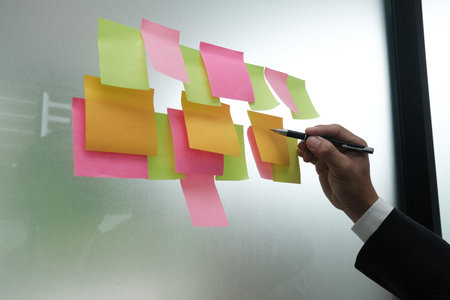 Businessman write on adhesive notes on glass wall at workplace. Sticky note paper reminder schedule...