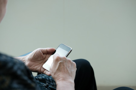 elder woman holding mobile phone. elderly senior female texting message, using app with smartphone at homeの写真素材