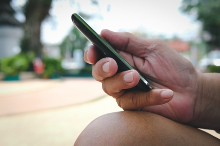 man holding mobile phone. hand texting message, using app with smartphone outdoorsの写真素材