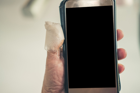 injured hand holding mobile phone with white adhesive bandage on thumbの写真素材