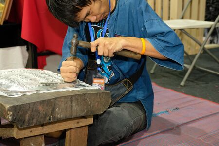Chiang Mai, Thailand - September 9, 2018: Silversmith craftsman carving pattern on silver plate, metal engraving at unseen lanna expo at Chiang Mai International Exhibition and Convention Centre in Chiang Mai, Thailand on September 9, 2018.のeditorial素材