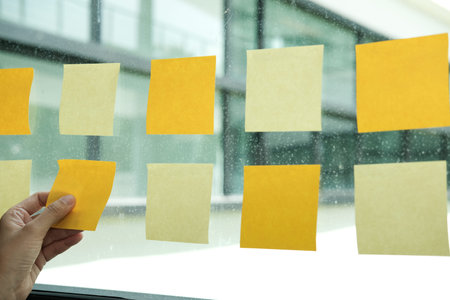 hand hold adhesive notes on glass wall at workplace. Sticky note paper reminder schedule for...