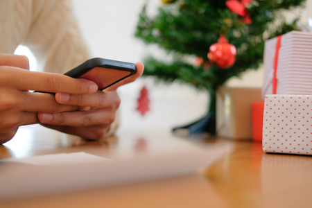 man wearing cream sweater using mobile smart phone with christmas decoration. xmas new year holiday celebration.の写真素材