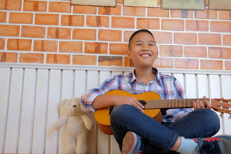 asian kid boy child playing guitar ukulele at home. children leisure activityの写真素材