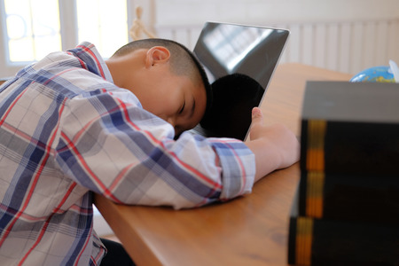 lazy stressed young little asian kid boy  resting sleeping on desk. child fall asleep. children tired from studying in classroom. childhood educationの写真素材
