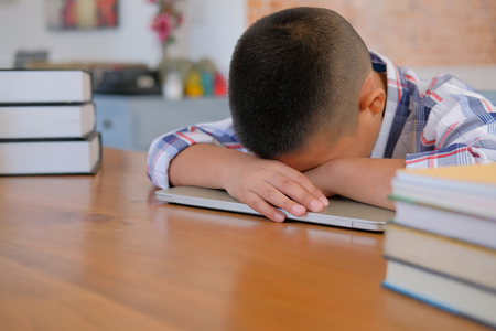 lazy stressed young little asian kid boy  resting sleeping on desk. child fall asleep. children tired from studying in classroom. childhood educationの写真素材