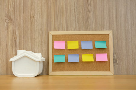 sticky notes paper reminder on cork board & house model on wooden desk. real estate investment. property buying mortgage loanの写真素材