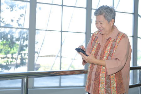 asian elder woman holding mobile phone on terrace. elderly female using smartphone on patio. senior texting message with cellphoneの写真素材