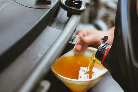 mechanic pouring oil to vehicle engine. serviceman changing motor oil in automobile repair service. maintenance and checkup in car garageの写真素材