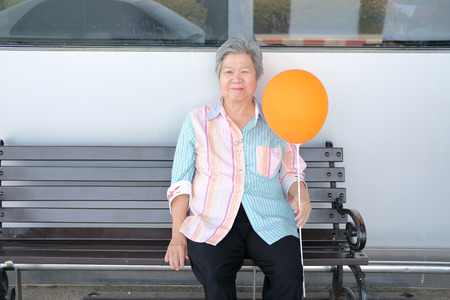 old elder woman holding balloon. asian elderly female relaxing outdoors. senior leisure lifestyleの写真素材