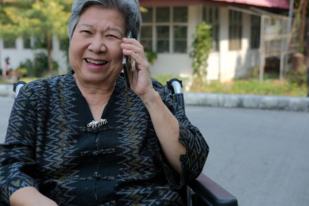 elder woman in wheelchair talk on mobile phone. elderly female speaking on smartphone. asian senior...