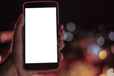 hand holding mobile smart phone with blank screen with bokeh night light background