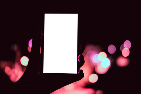 hand holding mobile smart phone with blank screen with bokeh night light background