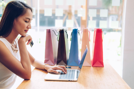 woman using computer & credit card for online payment with shopping bags on table. consumerism...