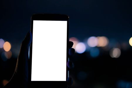 hand holding mobile smart phone with blank screen with bokeh night light backgroundの写真素材