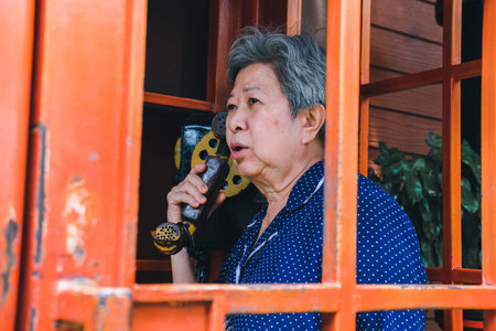 old elderly senior woman talking on vintage public telephone boothの写真素材