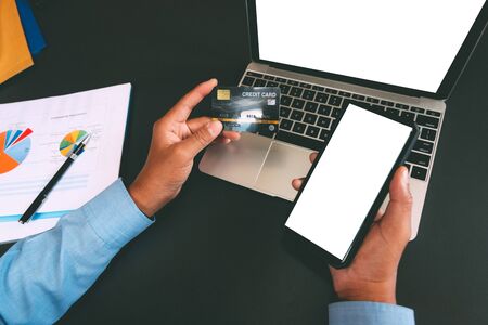 man holding credit card using smart phone for online shopping. businessman purchase product from internet, make payment on bank website at workplaceの写真素材