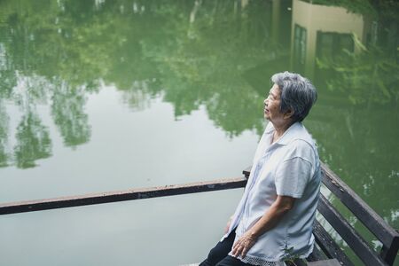 old elder woman resting near pond. asian elderly female relaxing outdoors. senior leisure lifestyleの写真素材