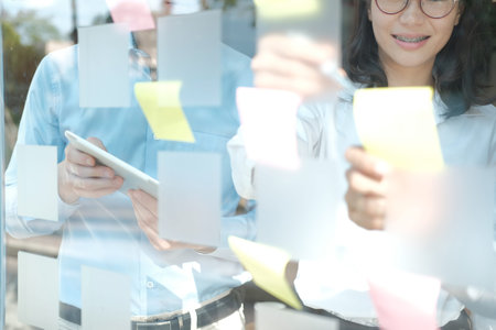 business people working planning discussing idea with sticky reminder note on glass wall at...