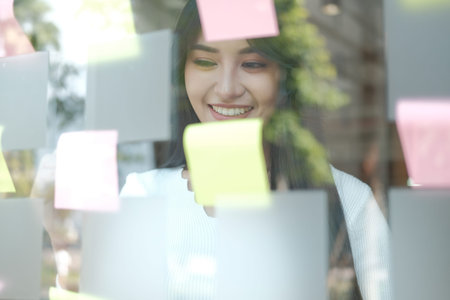 businesswoman woman thinking planning with adhesive notes on glass wall at workplace. Sticky note...