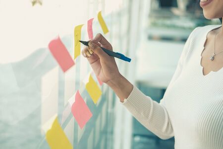 businesswoman woman thinking planning with adhesive notes on glass wall at workplace. Sticky note paper reminder schedule for creative idea & business brainstormingの写真素材