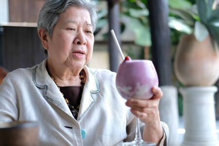 old asian elderly senior elder woman drinking berry smoothie milkshake at restaurant. mature retirement lifestyleの写真素材