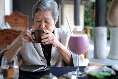 old elderly senior elder woman drinking coffee tea at restaurant. mature retirement lifestyleの写真素材