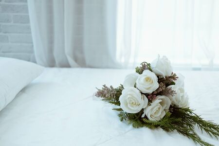 white bridal wedding rose flower bouquet on bed beside see through sheer window curtainの写真素材