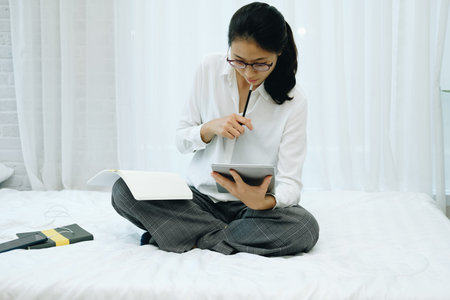 asian woman writing note watching video. student listen lecture study online course on bed in...
