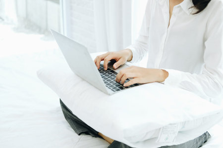 asian woman using computer laptop on bed in bedroom. work remotely  at home. leisure lifestyle