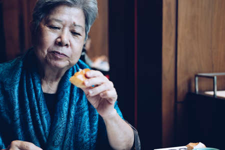 old asian elderly senior elder woman eating bread at restaurant. mature retirement lifestyleの写真素材