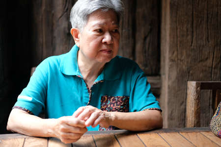 asian elderly female elder woman sitting near window at home. senior leisure lifestyleの写真素材