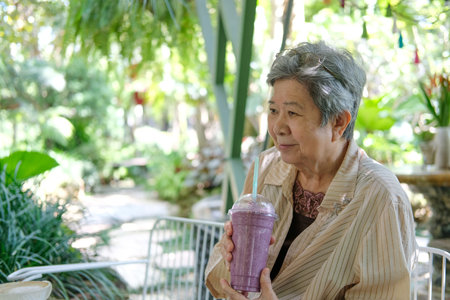 old asian elderly senior elder woman drinking berry smoothie yogurt milkshake at restaurant. mature...