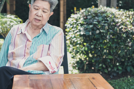 stressed depressed fatigued sad upset asian old asian elderly senior elder woman sitting in garden.の写真素材