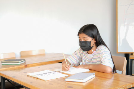 asian girl student wearing face mask studying writing notes doing homework in library. learning...