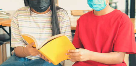 asian boy girl student wearing face mask studying reading book in library. learning education at schoolの写真素材