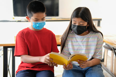 asian boy girl student wearing face mask studying reading book in library. learning education at...