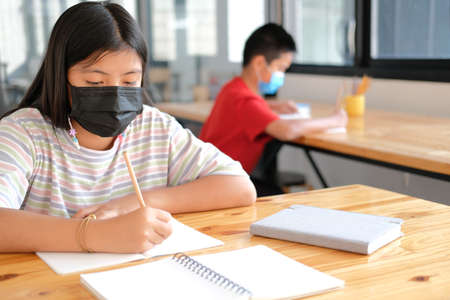 asian girl student wearing face mask studying writing notes doing homework in library. learning education at schoolの写真素材