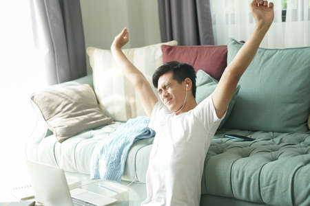 asian young student man teenager entrepreneur wear earphones stretching feeling tired bored sleepy while working with computer studying learning online at home. e-learning educationの写真素材