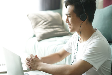 asian young teenage student man entrepreneur wear headphones working by video call conference studying learning online at home.の写真素材