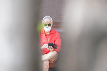 asian old elder senior man elderly male wearing face mask using mobile smart phone cellphone...